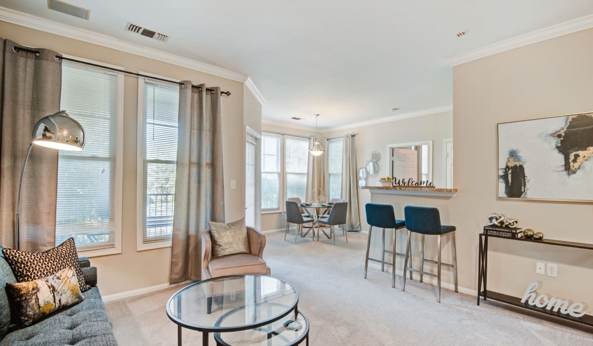Living room and dining area of an open concept model apartment and Kitchen with island and bar stools, at Village at Potomac Falls Apartment Homes in Sterling, Virginia
