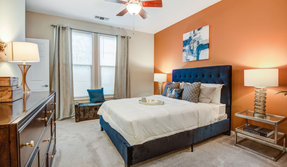 Spacious bedroom with large comfortable bed, desk, and large window at Village at Potomac Falls Apartment Homes in Sterling, Virginia